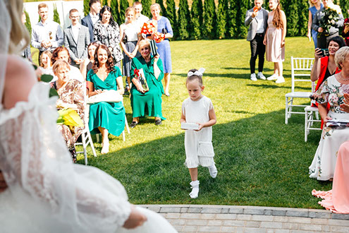 Маленькая девочка ангел несет свадебные кольца на церемонии бракосочетания.