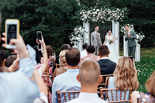 Гости на свадьбе фотографируют на мобильные телефоны первый поцелуй жениха и невесты.